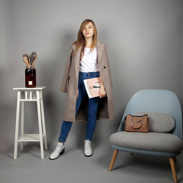 Pretty young blonde european girl at grey coat posing on camera.studio shooting at grey background - Fotoğraf, Görsel