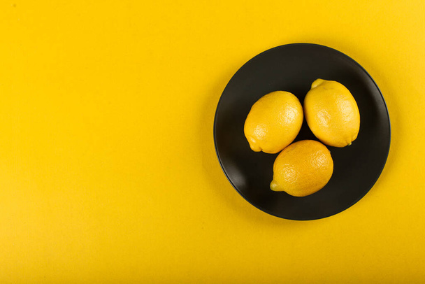 Limones en un plato en el lado derecho sobre un fondo amarillo
 - Foto, imagen