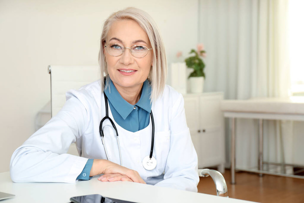 Portrait of mature female doctor in white coat at workplace - Foto, Bild