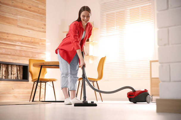Young woman using vacuum cleaner at home - Valokuva, kuva