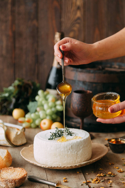  A large white round cheese on a plate. Curd cheese is watered with honey. The chef's hands prepare cheese. - Zdjęcie, obraz