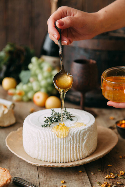  A large white round cheese on a plate. Curd cheese is watered with honey. The chef's hands prepare cheese. - Foto, Imagem