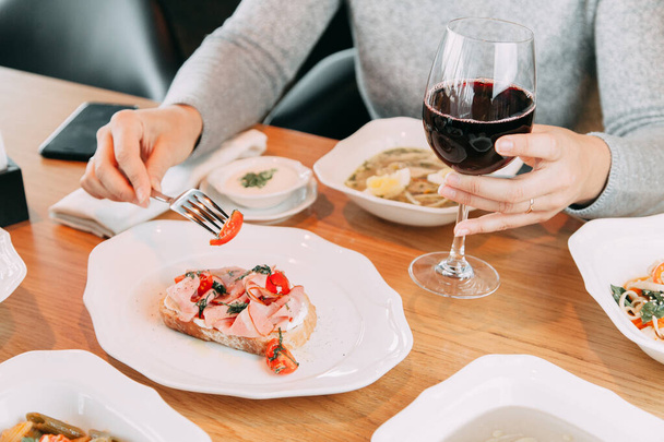Restaurant dish on the menu with wine. The girl is eating bruschetta with bacon and tomato.  - Foto, imagen