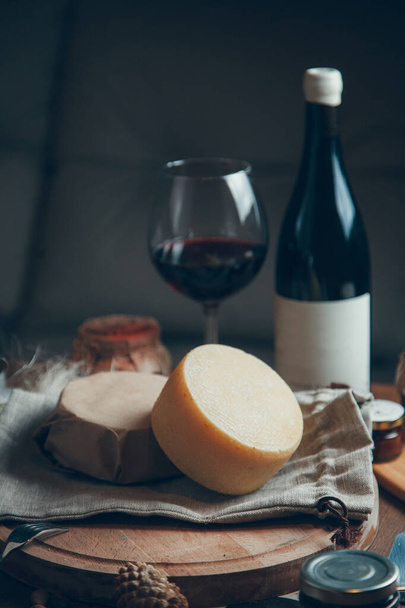 A smooth circle of hard cheese with wine and a glass. Farm cheeses on a wooden Board. Still life with hard sliced cheese.  - Foto, immagini