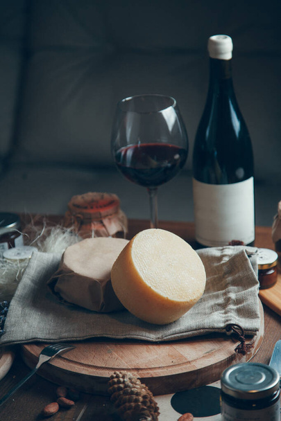 A smooth circle of hard cheese with wine and a glass. Farm cheeses on a wooden Board. Still life with hard sliced cheese.  - Photo, image