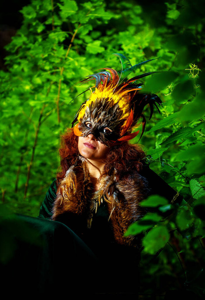 chica con máscara de plumas chamánica y vestido histórico en los alrededores del bosque
 - Foto, Imagen