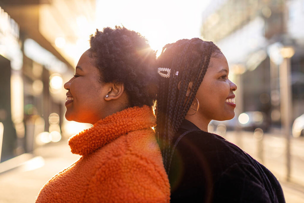 Two beautiful Afro american women standing back to back in city - Zdjęcie, obraz