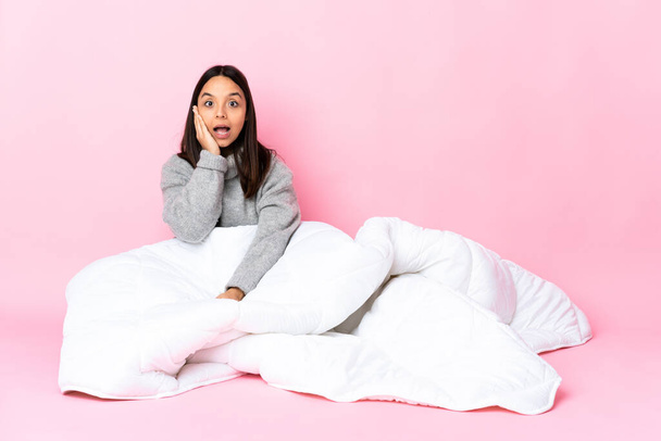 Young mixed race woman wearing pijama sitting on the floor with surprise and shocked facial expression - Photo, Image