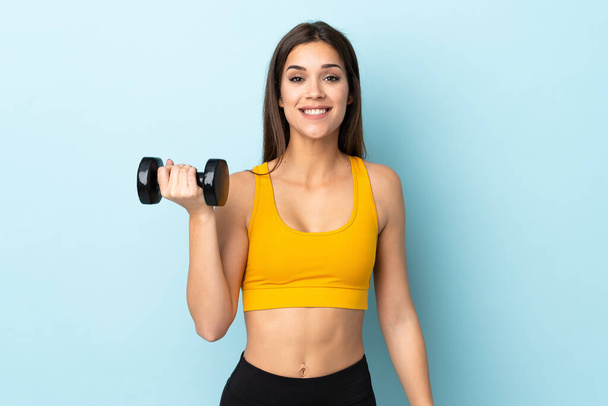 Young caucasian woman making weightlifting isolated on blue background with surprise and shocked facial expression - Photo, Image
