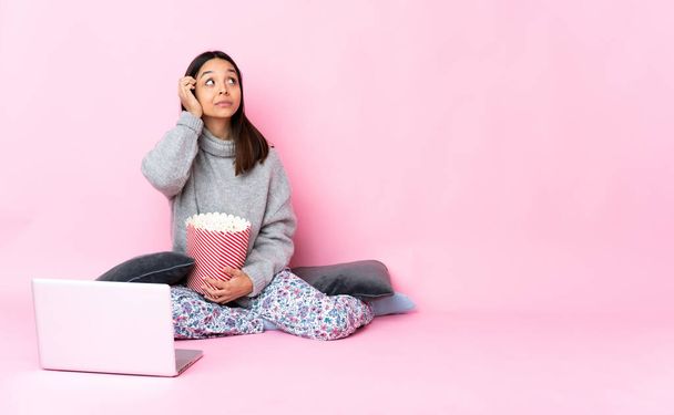 Νεαρή γυναίκα μικτή φυλή τρώει ποπ κορν, ενώ βλέποντας μια ταινία στο φορητό υπολογιστή έχοντας αμφιβολίες και τη σκέψη - Φωτογραφία, εικόνα
