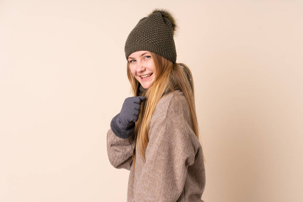 Teenager ukrajinský dívka s zimní klobouk izolované na béžové pozadí slaví vítězství - Fotografie, Obrázek