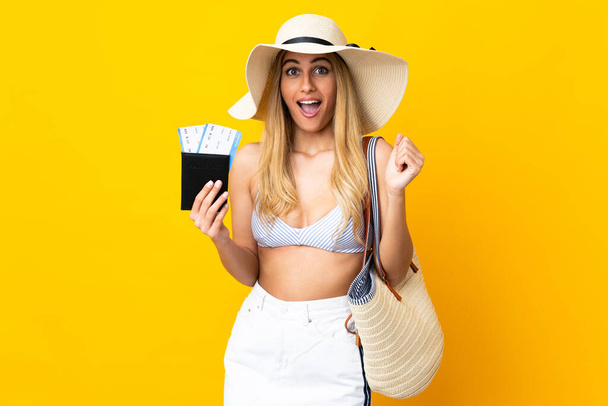 Jeune femme blonde uruguayenne en maillot de bain tenant un passeport sur fond jaune isolé avec une expression faciale surprise et choquée - Photo, image