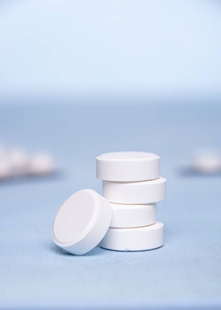 Vitamin C tablets are grouped in vertical pile on blue surface. One tablet is at the bottom of  pile. Two unfocused blister packs at background. Selective focus. Vertical background with copy space. - Foto, Imagen