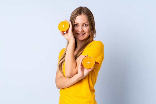 Teenager Ukrainian girl isolated on blue background holding an orange - Fotó, kép