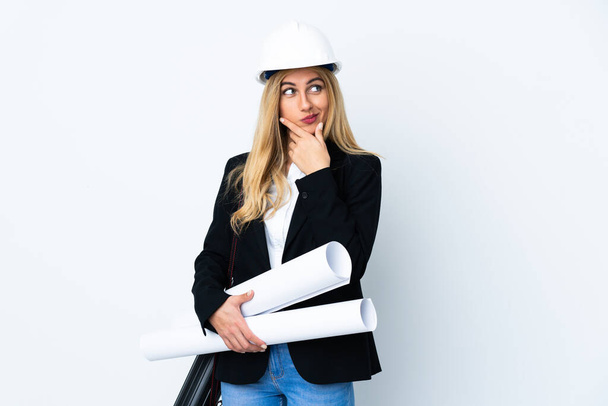 Giovane donna architetto con casco e tenendo cianografie su sfondo bianco isolato pensando un'idea - Foto, immagini