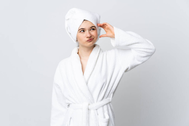 Menina adolescente em um roupão de banho isolado no fundo branco com dúvidas e com expressão facial confusa
 - Foto, Imagem