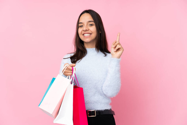 Mladá žena s nákupní taškou přes izolované růžové pozadí ukazuje a zvedá prst ve znamení toho nejlepšího - Fotografie, Obrázek