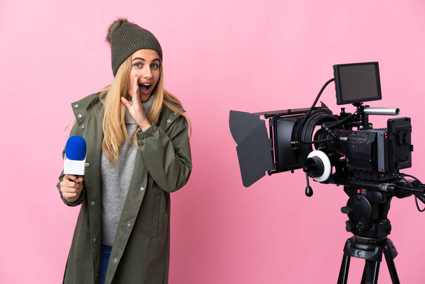 Reporterin hält ein Mikrofon in der Hand und berichtet über isolierten rosa Hintergrund, der zur Seite zeigt, um ein Produkt zu präsentieren, und flüstert etwas - Foto, Bild