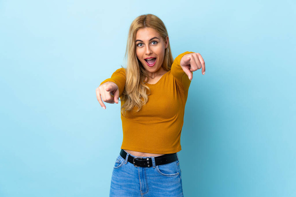 Young Uruguayan blonde woman over isolated blue background surprised and pointing front - Foto, Bild
