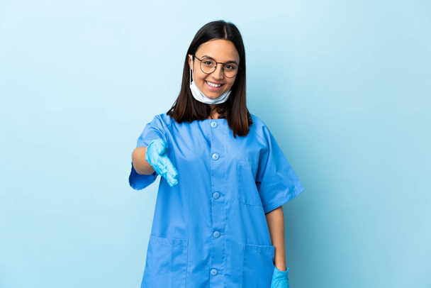 Surgeon woman over isolated blue background shaking hands for closing a good deal - Fotografie, Obrázek