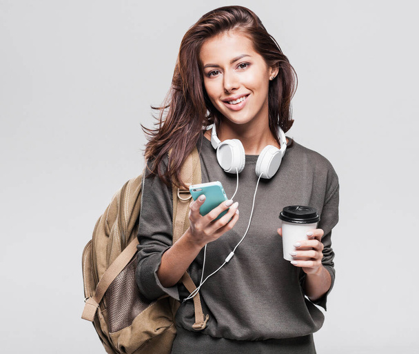Young beautiful woman with backpack holding smartphone and coffee cup - Фото, изображение