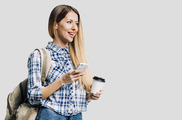 Young beautiful woman with backpack holding smartphone and coffee cup - Φωτογραφία, εικόνα