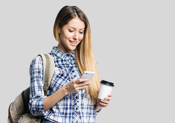 Mladá krásná žena s batohem drží smartphone a šálek kávy - Fotografie, Obrázek