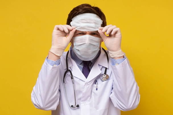 Médico o médico posando con varias mascarillas aisladas sobre fondo amarillo. Protección incorrecta contra la gripe o el virus covid-19
. - Foto, imagen