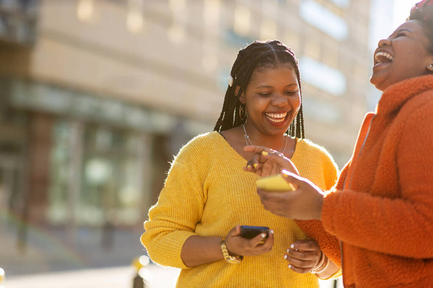 Щасливі друзі-жінки відправляють повідомлення зі своїми смартфонами в місті
 - Фото, зображення