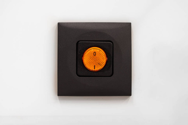 Leuchtend orange elektrische Schalter auf braunem Gehäuse Nahaufnahme Frontalaufnahme isoliert auf grauem Hintergrund 2020 - Foto, Bild