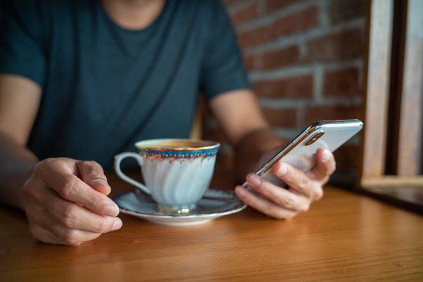 Бізнесмен використовує смартфон під час пиття гарячої латеної кави в кав'ярні
 - Фото, зображення