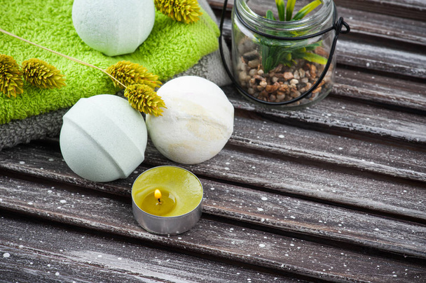 Aroma bath bombs, green towels and succulents in SPA arrengement on brown wooden table. Lit candle with dry flowers - Foto, afbeelding