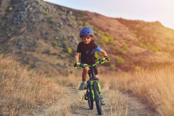 Щасливий хлопчик 7 років веселиться в осінньому парку з велосипедом в прекрасний осінній день. Активна дитина в шоломі велосипеда
 - Фото, зображення