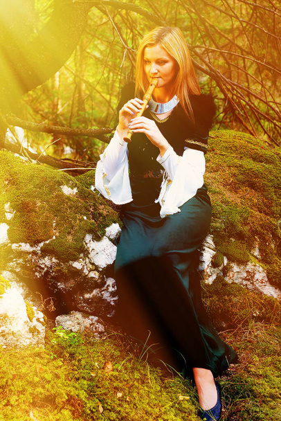 krásná dívka v historickém kostýmu hraje na flétnu v lese. Světelný efekt - Fotografie, Obrázek