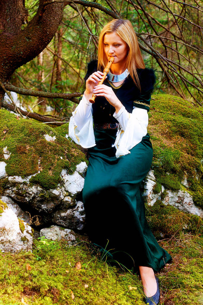 krásná dívka v historickém kostýmu hraje na flétnu v lese. a světlý grafický efekt - Fotografie, Obrázek