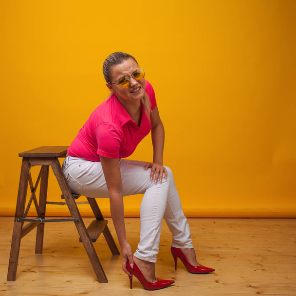 young woman suffers from uncomfortable high-heeled shoes, portrait in the Studio on a yellow background. - Foto, imagen