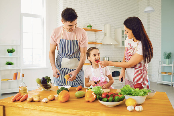 Mutfakta salata yapan taze sebzeli bir masada gülümseyen mutlu bir aile.. - Fotoğraf, Görsel