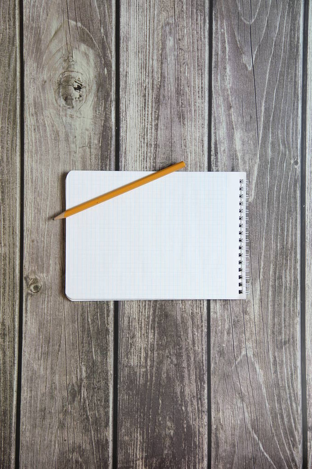 Bloc de notas con una hoja blanca en blanco en un papel de damero con lápiz de grafito simple se encuentra en el fondo de las tablas de madera
 - Foto, imagen
