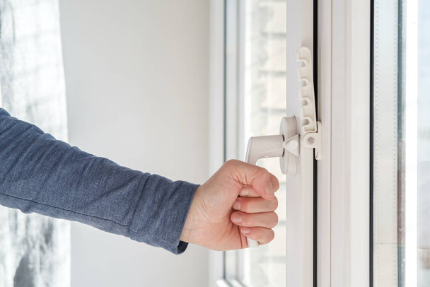 Main féminine fermé une fenêtre moderne en PVC blanc, avec un dispositif de fixation attaché pour la ventilation, à la lumière naturelle
. - Photo, image