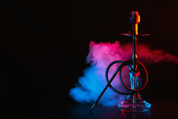 hookah with a glass flask and a metal bowl shisha with colored smoke on the table - Photo, Image
