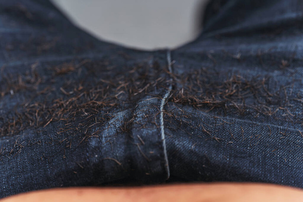 Rasierte Haare zu blauen Jeans. Menschlich geschnittenes Haar mit Bart auf dunklem Hintergrund. Kleine Haare auf der Kleidung abgeschnitten - Foto, Bild