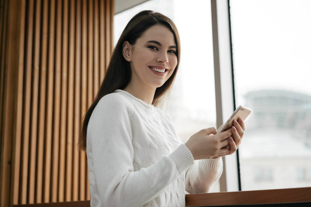 Beautiful caucasian woman using mobile phone, communication, shopping online. Happy girl holding smartphone, ordering food, booking tickets, looking at camera and smiling - Photo, Image