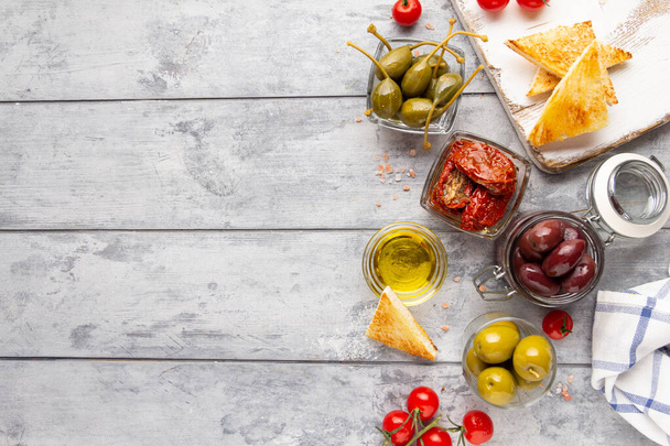 Italian antipasti, olives, capers, sun- dried tomatoes , olive oil, bread (ciabatta, baguette, croutons). Mediterranean assortment of delicious food, wine snacks - Photo, Image