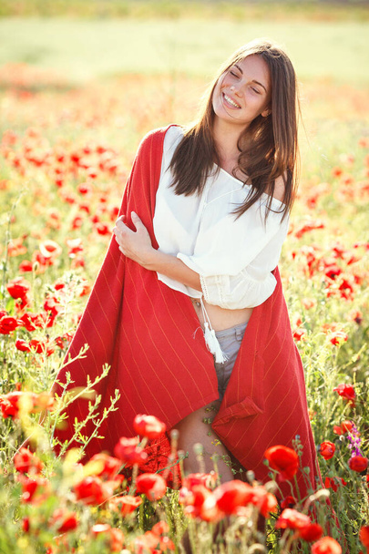 young beautiful woman walking through a poppy field in summer. Close up portrait of lovely young romantic woman posing on field background. Soft colors. - Photo, Image