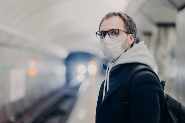 Coronavirus crisis. Male follows quarantine rules wears protective medical mask, travels in public transport cares about health during epidemic or pandemic. Danger of catching virus in city transport - Valokuva, kuva