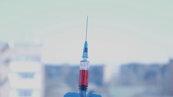 Střelba injekční jehly s kapkou krve na okénka na pozadí ve městě - Záběry, video