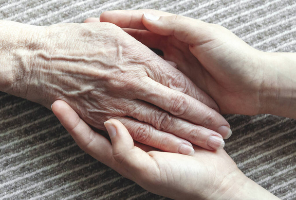Młode dłonie trzymające starą kobietę za rękę, zbliżenie - Zdjęcie, obraz