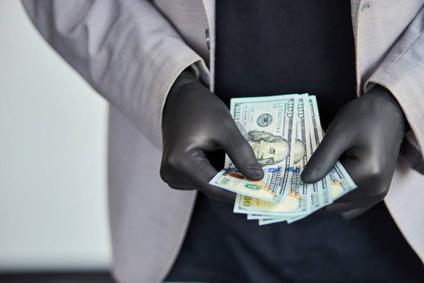 Facet trzymający w ręku pieniądze w czarnych rękawiczkach medycznych. Kryzys koronawirusowy. Oszczędność pieniędzy. - Zdjęcie, obraz
