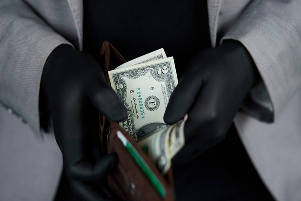 Facet trzymający portfel z pieniędzmi w ręku w czarnych rękawiczkach medycznych. Kryzys koronawirusowy. Oszczędzaj pieniądze. Nie męski. Kryzys światowy - Zdjęcie, obraz