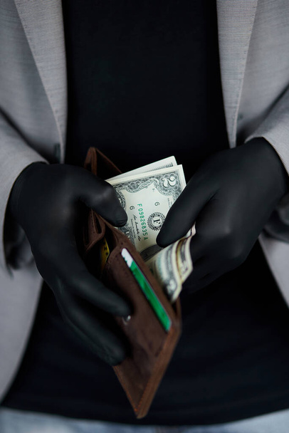 Een man met een portemonnee met geld in zijn hand in zwarte medische handschoenen. Coronaviruscrisis. Bespaar geld. Geen mannelijkheid. De wereldcrisis - Foto, afbeelding